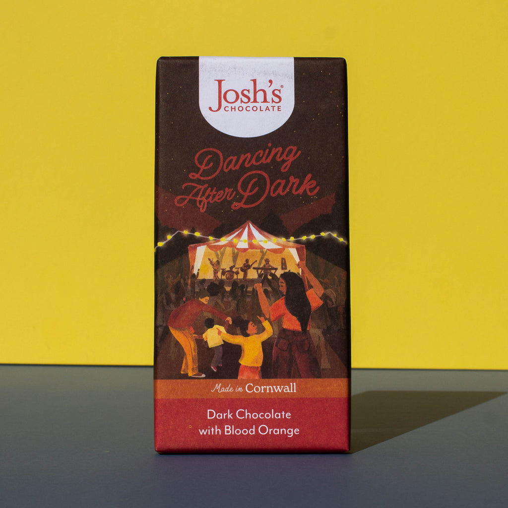 Bar of Josh's Dark Chocolate with Blood Orange, it is a dark orange and red paper wrapper with an illustration of an outdoor music event, it is placed on a blue and yellow background.