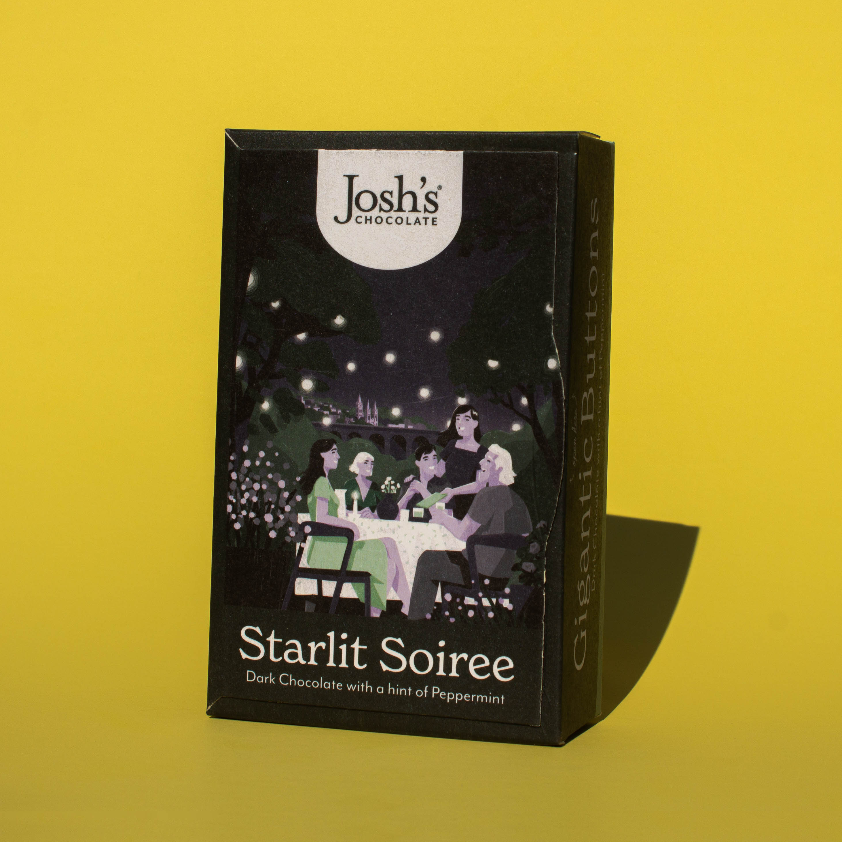 Box of Josh's Dark Chocolate Peppermint Buttons tilted to the side, it is a black box an with illustration of a late night gathering of friends, it is placed on a yellow background.