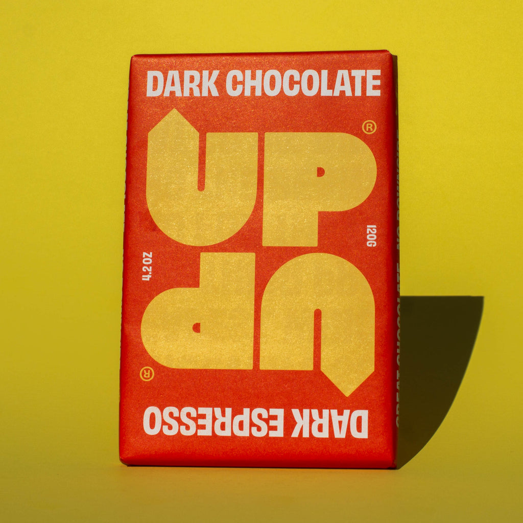 Bar of UP UP Dark Espresso Dark Chocolate, it has a red paper wrapper with a yellow logo, it is placed on a yellow background.