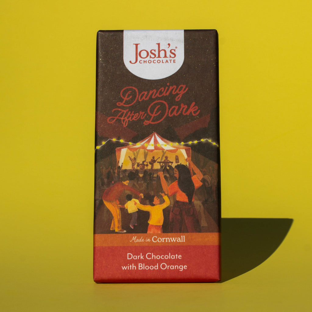 Bar of Josh's Dark Chocolate with Blood Orange, it is a dark orange and red paper wrapper with an illustration of an outdoor music event, it is placed on a yellow background.