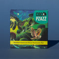 Bar of Coco Pzazz Roasted Hazelnut Milk chocolate, it has a dark blue wrapper with an illustration of an owl flying over farmland, it is placed on a blue background.